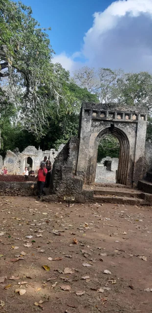 L'arco in pietra all'ingresso di un sito storico, con alcuni visitatori sotto gli alberi.